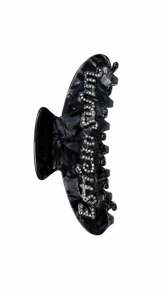 Estrella Swim black hair claw clip with rhinestone logo on white background.