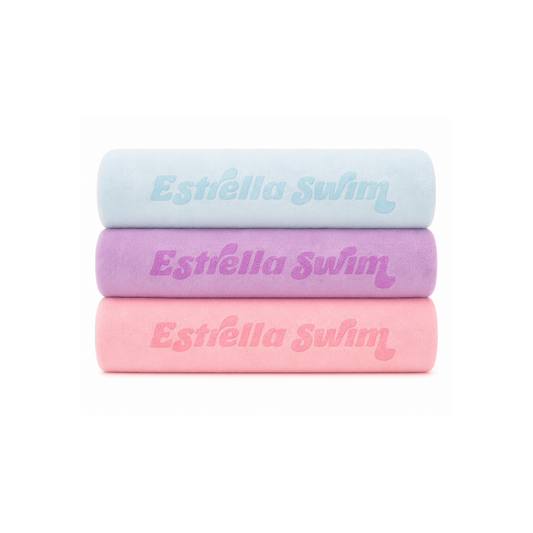 Estrella Swim microfiber beach towels in baby blue, purple, and pink.